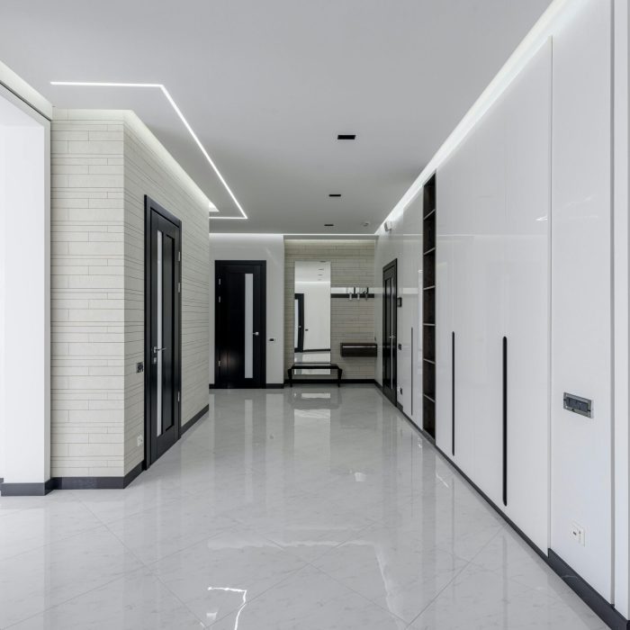 Spacious corridor of modern apartment with white walls dark doors and LED highlighting on ceiling